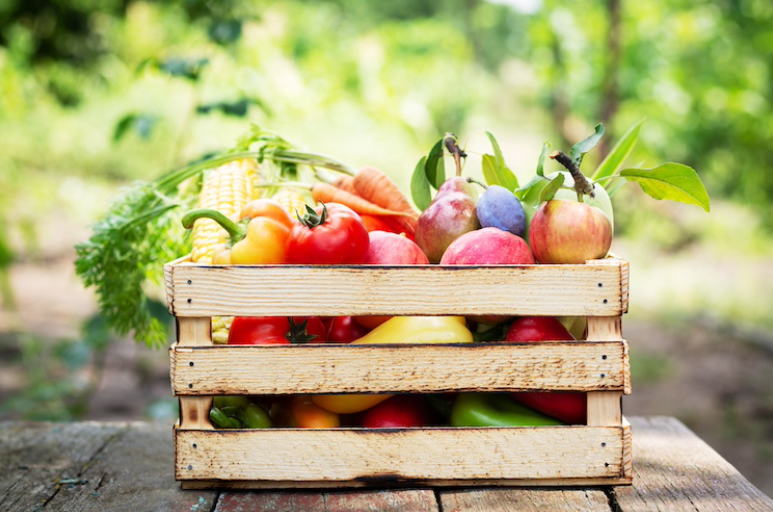 Caja de fruta de madera llena de verduras como pimientos, con un fondo de vegetación