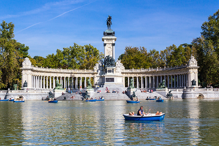 Imagen del monumento a Alfonso XII (estatua de un hombre sobre un caballo a gran altura, rodeada de columnas) en el Parque del Retiro, con un estanque y barcas delante