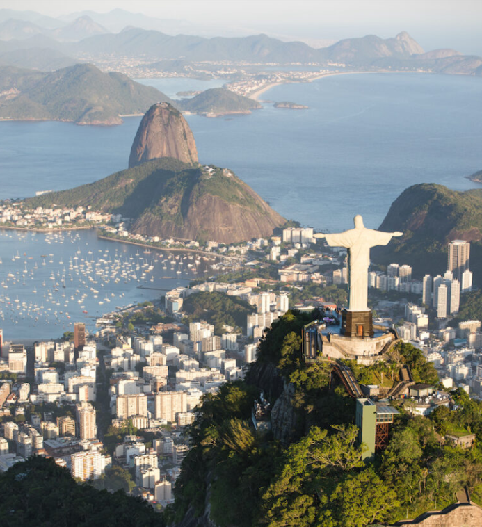 Imagen de la estatua del Cristo redentor con los brazos abiertos sobre una colina verde, con la ciudad debajo y el mar