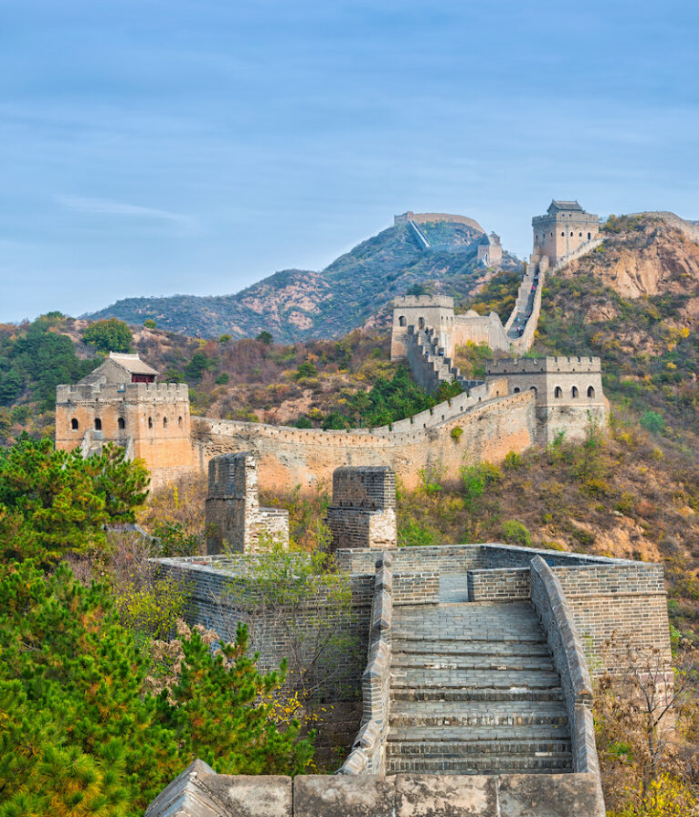Imagen de la Gran Muralla China, rodeada de vegetación, serpenteando por la montaña